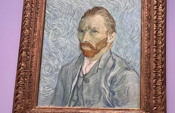 A framed painting of a man with reddish-brown hair and beard, wearing a blue coat, against a swirling blue background.