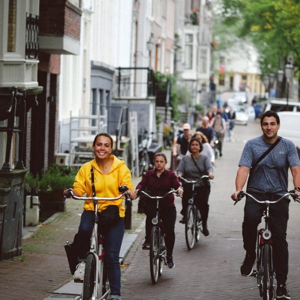 A group of people ride bicycles along a residential street lined with parked cars and trees.
