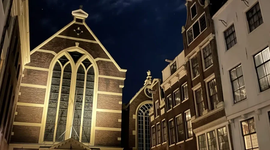 A church and surrounding buildings are illuminated at night under a partly cloudy sky with the moon visible above. A church and surrounding buildings are illuminated at night under a partly cloudy sky with the moon visible above.