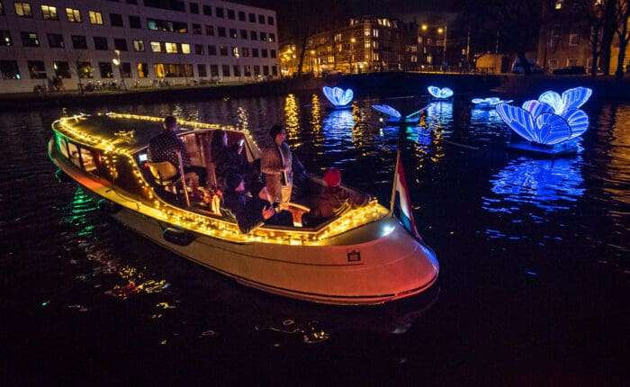 Canal boat with guests passing glowing butterfly light artworks at Amsterdam Light Festival